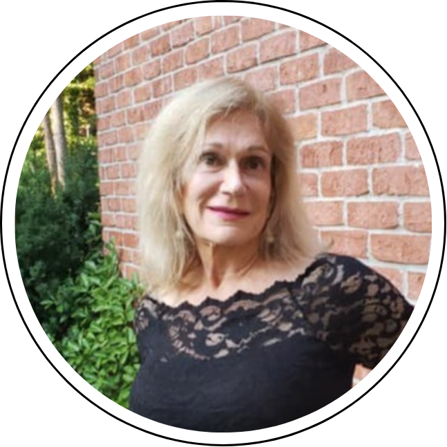 Linda Rickles profile: A woman with blonde hair wearing a black lace top stands in front of a brick wall with greenery in the background, representing a leading luxury interior designer in Atlanta.